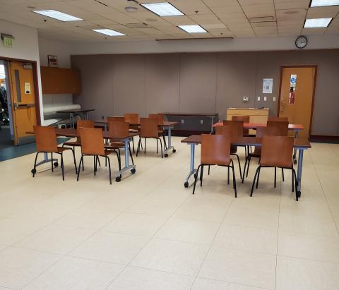 large room set up with multiple tables, wooden chairs, and projector screen