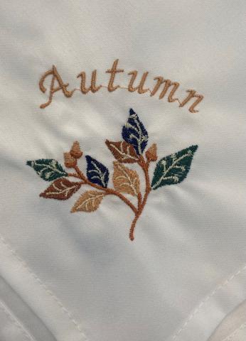 A napkin with embroidered autumn leaves and the word "Autumn" curved above them