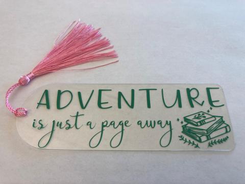 acrylic bookmark with vinyl decoration that says "adventure is just a page away"