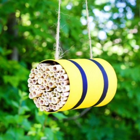 yellow can with filling for bee homes, hanging from twine and greenery in background