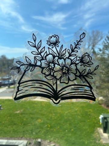 Suncatcher window cling that pictures a book with flowers coming out of it