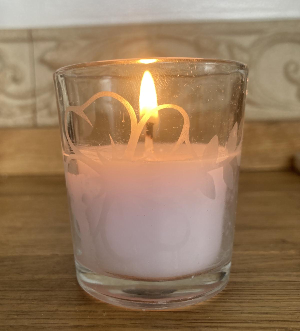 Lit glass votive candle with etched glass design.