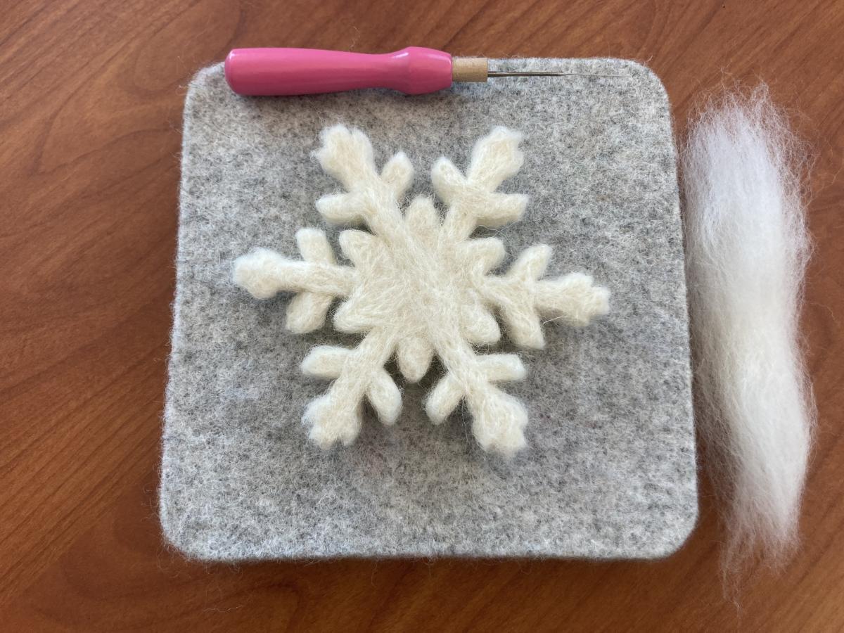 Needle felted snowflake with wool and a felting needle next to it.