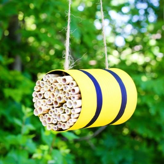 yellow can with filling for bee homes, hanging from twine and greenery in background